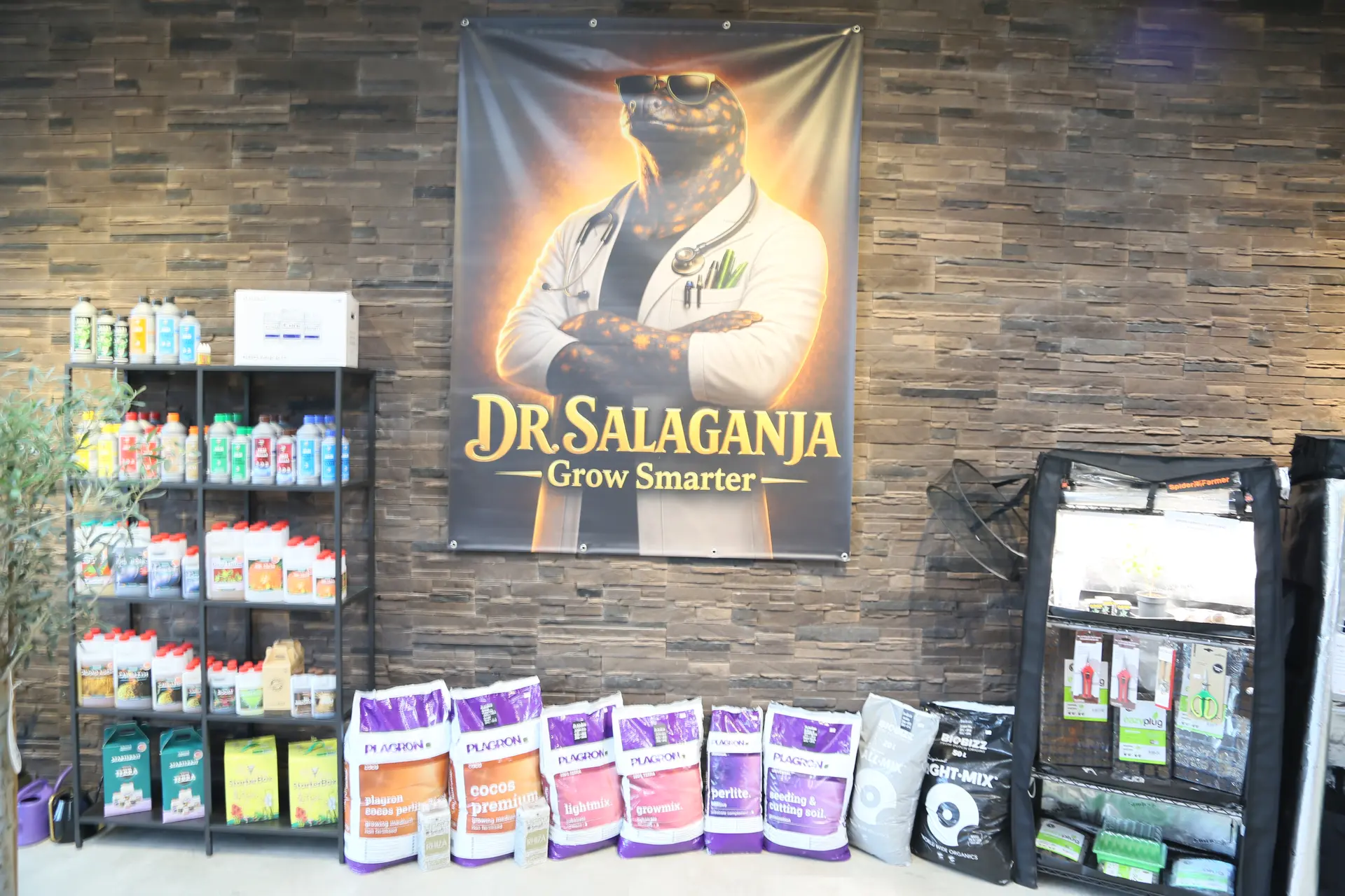 Regalwand mit Flaschen und Zubehör unter einem Dr.-Salaganja-Banner, davor Säcke mit Erde, daneben ein Growzelt