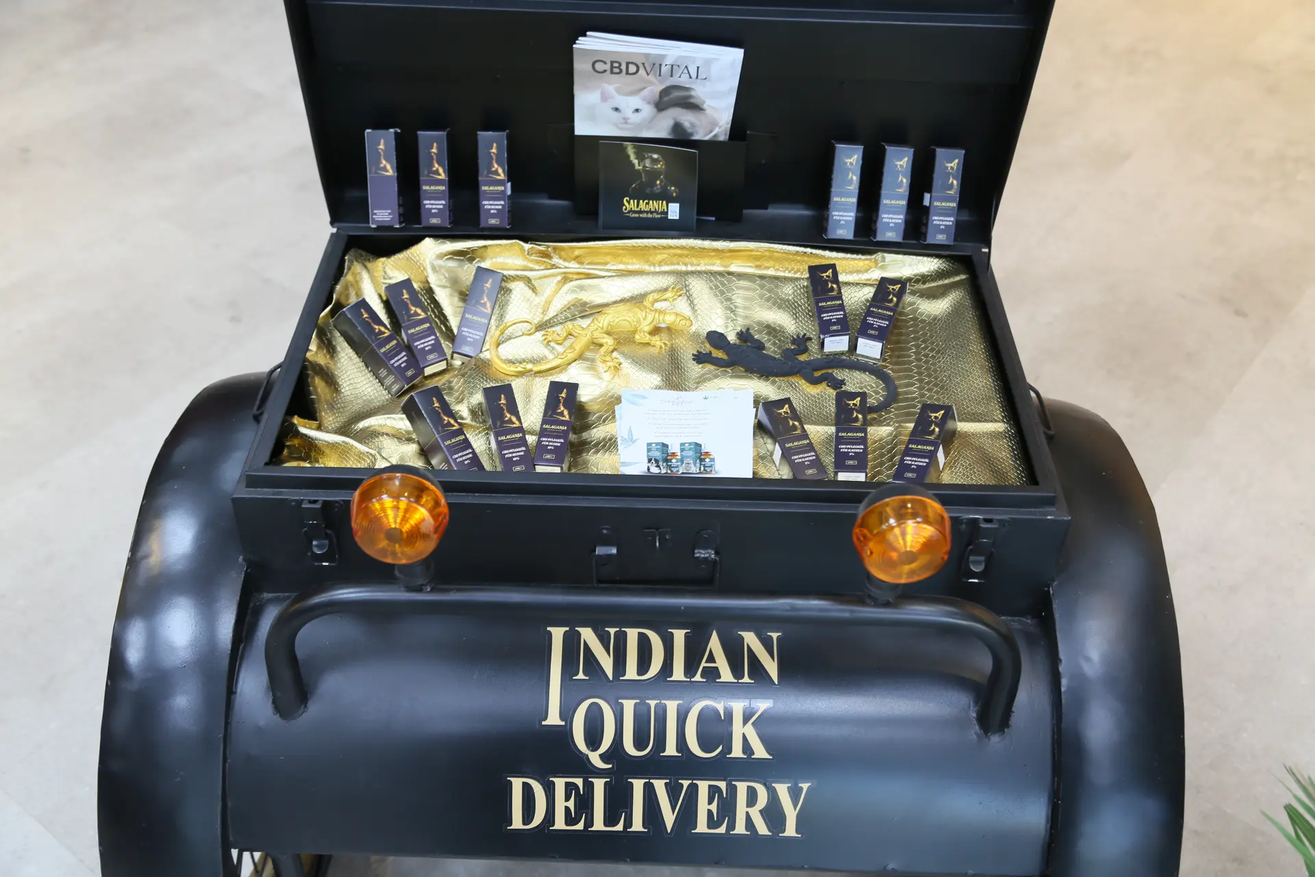 Schwarzer Wagen „Indian Quick Delivery“ mit offenem Deckel, innen golden ausgekleidet, mit kleinen Schachteln und zwei Gecko-Figuren