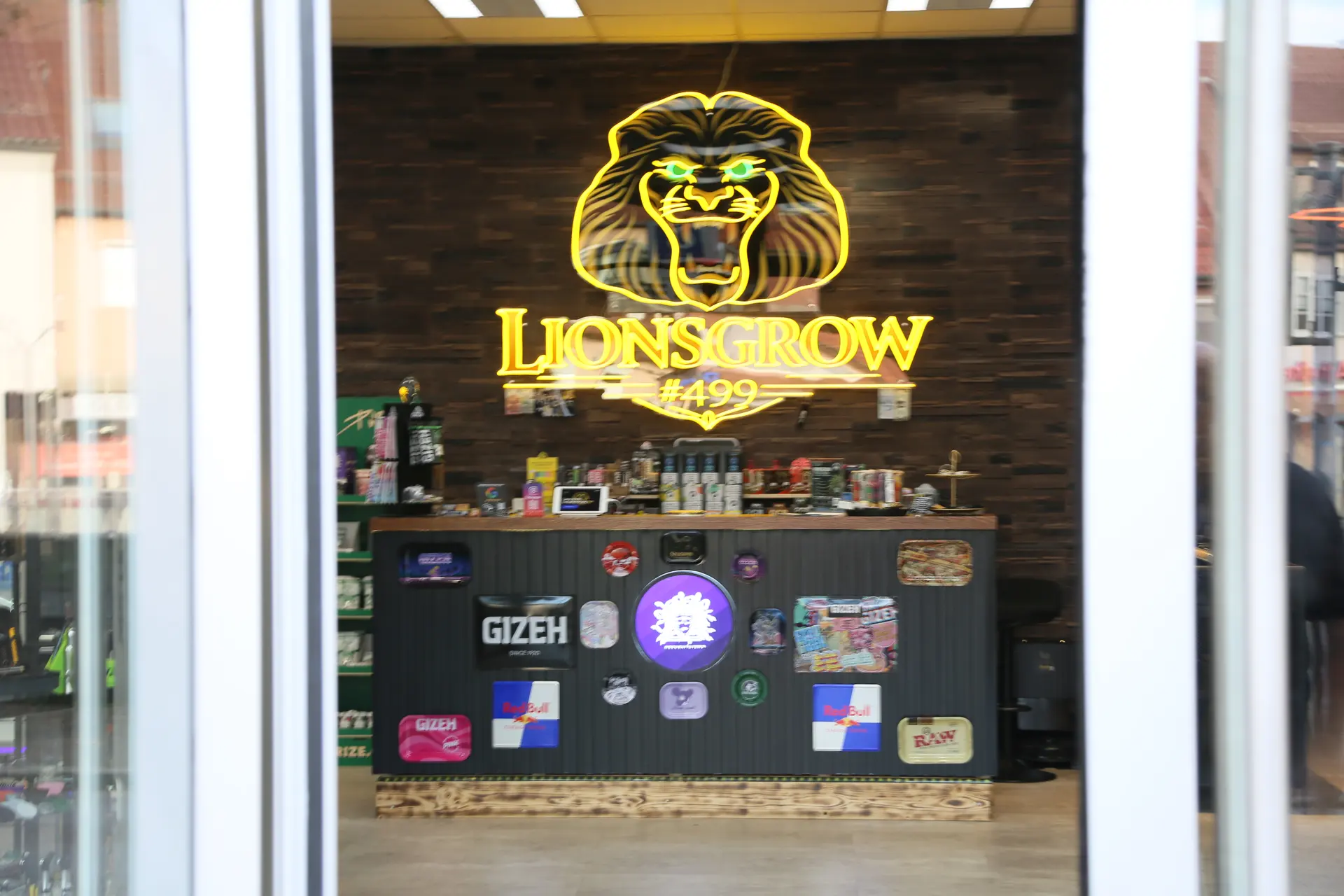 Blick durch die Glastür auf das beleuchtete Lionsgrow-Logo an der Backsteinwand